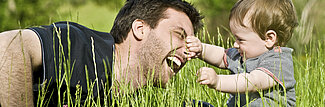 Vater und Kind in der Wiese, Kind hält spielerisch die Nase des Vaters fest