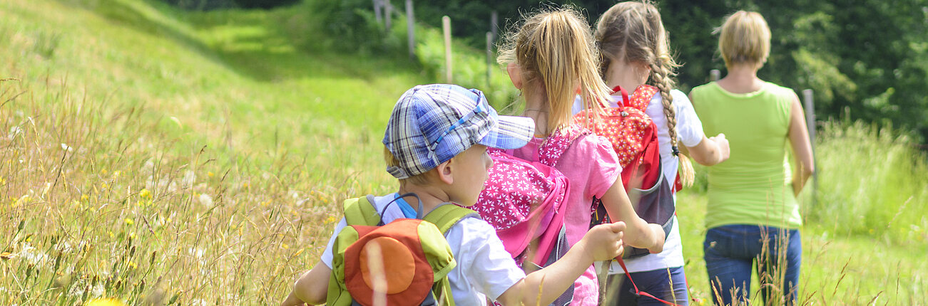 Kinder gehen eine Wanderung über eine Wiese.